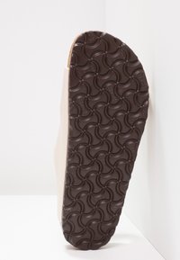 Skor med en beige ovandel och en texturerad brun gummisula som har ett vågigt mönster för bra grepp. Designen är minimalistisk och strukturerad.