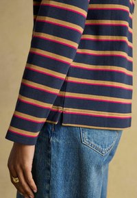 Tumesinise pikakäisega särk horisontaalse kuld- ja roosade triipudega. Omab ümmargust äärt ja nähtavaid õmblusdetailide.