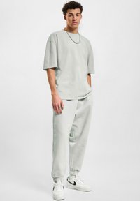 Camiseta de gran tamaño color gris claro y pantalones de chándal a juego, con puños elásticos y bolsillos laterales, combinados con zapatillas blancas con detalles negros.