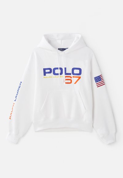 Balta kapucēta džemperis, kurā izšūta "POLO 67" zilā un oranžā krāsā, ar "RALPH LAUREN" zilo uz piedurknes un Amerikas karoga uzšuvumu.