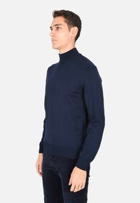 Maglione a dolce vita blu navy realizzato in un tessuto liscio e morbido, con maniche lunghe e un design aderente che arriva ai fianchi.