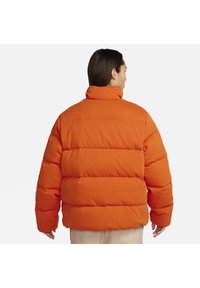 Orangene Pufferjacke mit hohem Kragen, gestepptem Design in horizontalen Streifen und lässiger Passform. Weiche Textur mit elastischen Bündchen.