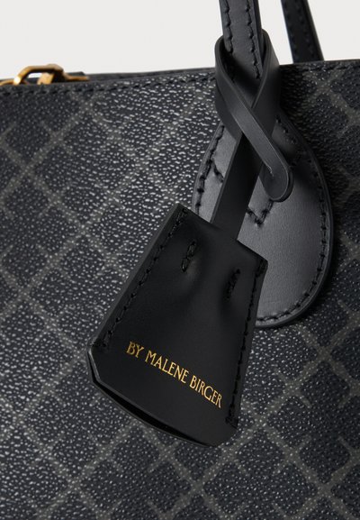 Gros plan d'un sac à main noir texturé avec une étiquette en cuir attachée, affichant un texte doré "BY MALENE BIRGER" sur l'étiquette.