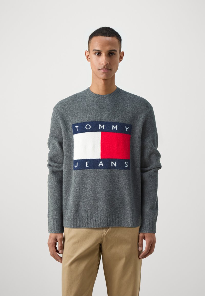 Maglione grigio lavorato a maglia con design del logo rettangolare in blu navy, rosso e bianco con il testo "TOMMY JEANS", collo rotondo e polsini a coste.