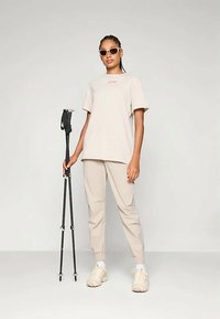 Bežs T-krekls un sašaurināti bikses, abi izgatavoti no viegla auduma. Aksesuāri ietver saulesbrilles un melnu pastaigu nūju, kā arī neitrālas sporta apavus.