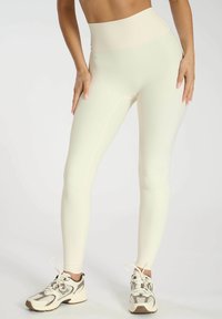 Leggings côtelés taille haute d'un beige clair avec une texture lisse et une coupe près du corps. Associés à des baskets de sport de couleur claire.