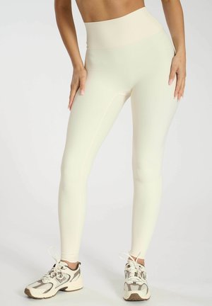 Leggings a vita alta in maglia di un cremoso pallido, con una consistenza liscia e una vestibilità aderente. Abbinati a scarpe da ginnastica di colore chiaro.