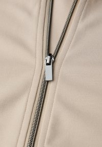 Giacca beige con zip, dalla texture liscia, con cerniera metallica argentata e tiretto dritto.