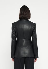 Čierny kožený blejzer s priliehavým strihom, hladkou textúrou a ostrými klopami. Má strihané švy a gombíkové manžety.