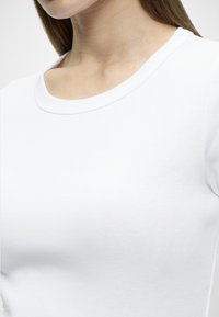 Λευκό βαμβακερό T-shirt με στρογγυλή λαιμόκοψη, εφαρμοστή γραμμή και ριμπ υφή, παρουσιάζοντας έναν ομαλό, απλό σχεδιασμό.