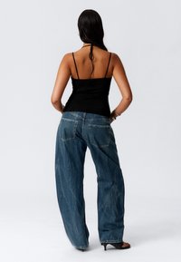 Schwarzes, tailliertes Tanktop mit dünnen Trägern, kombiniert mit lockeren blauen Denim-Jeans, die zwei hintere Taschen und sichtbare Nähte aufweisen.