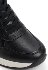 Svart lädersneaker med en slät yta, rund tå och vit mellansula; har svarta snören och noggrant sydda detaljer.