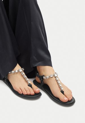Black flat sandals with a T-strap design, featuring clear rectangular gems along the strap and a smooth rubber sole.