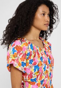 Blomstrete kjole med et livlig mønster i rosa, blått, oransje og gult, korte ermer, rynket hals og elastisk midje.