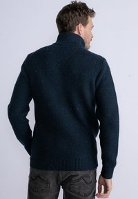 Pulover tricotat de culoare albastru închis, cu guler înalt, model texturat și manșete și tiv cu nervuri. Vedere din spate; detalii vizibile ale umerilor și brațelor.