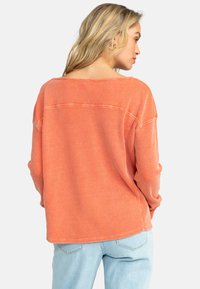 Pitkähihainen, löyhkähihainen paita teksturoidusta oranssista kankaasta, leveällä pääntiellä ja lasketuilla harteilla, jossa on hienovarainen ribbineuloskuvio.