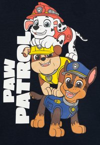 Paw Patrol Themen Grafik mit drei Cartoon-Hunden: einem schwarz-weiß gepunkteten Hund mit rotem Feuerwehrhelm, einem braunen Hund in gelber Weste und einem braunen Hund in blauer Polizeiuniform.