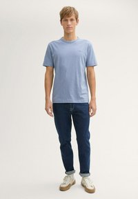 Tricou cu mânecă scurtă de culoare albastru deschis, realizat dintr-un material moale, asortat cu blugi de culoare albastru închis și teniși bej, având manșete rulificate.