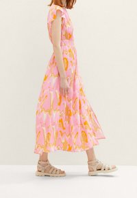 Abito maxi rosa con motivi astratti arancioni e beige, maniche a volant corte e vita arricciata, abbinato a sandali beige con cinturini.