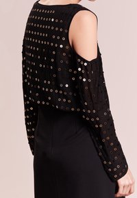 Top cropped nero con dettagli metallici a occhiello, maniche lunghe e aperture sulle spalle, abbinato a una gonna nera elegante.