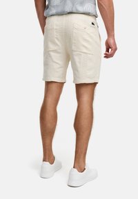Beige Baumwollshorts mit strukturiertem Finish, zwei Gesäßtaschen und geradem Schnitt, kombiniert mit weißen Sneakers.