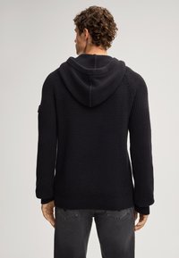 Czarna dzianinowa bluza z kapturem o strukturalnym wzorze, z prążkowanymi mankietami i luźnym krojem. Posiada duży kaptur i prosty dół.