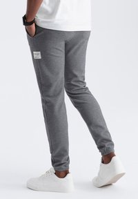Joggers grises confeccionados con una tela suave, que presentan un corte ajustado, puños elásticos y una pequeña etiqueta blanca en el costado. Combinados con zapatillas blancas.