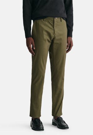 Olive green chinos with a straight fit, flat front, and belt loops, paired with black loafers. Soft cotton material with a smooth texture.