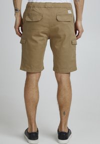 Tan cargoshorts med elastisk midja, två bakfickor och sidofickdetalj. Tillverkade av ett lätt tyger. Skorna är svarta.