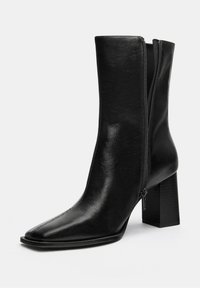 Crne gležnjače s šiljastim vrhom, glatkom sintetičkom kožom, zatvaranjem na bočnoj strani i debelim blok petama.