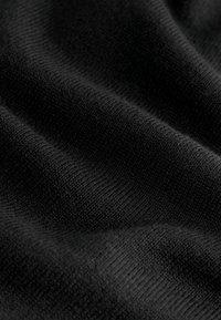 Vue en gros plan d’un tissu tricoté noir avec des plis doux et des détails de texture visibles.