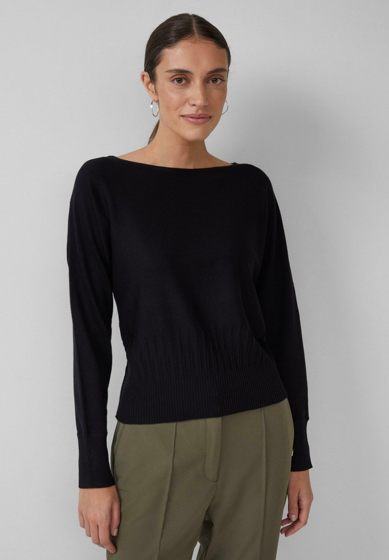 Schwarzer Pullover mit weitem Ausschnitt, langen Ärmeln und geripptem Saum. Glatte Textur, tailliert geschnitten, kombiniert mit olivgrünen Hosen.