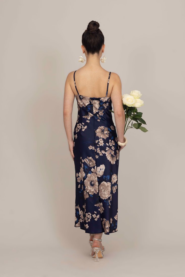 Vestito slip in satin con motivo floreale in blu navy, caratterizzato da spalline sottili, una silhouette aderente e un design di lunghezza media, accessorato con un bouquet.