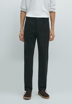 Zwarte chino's met een recht model, gemaakt van een gladde stof. Beschikt over een knoopsluiting en zijzakken, gecombineerd met een paar bruine schoenen.