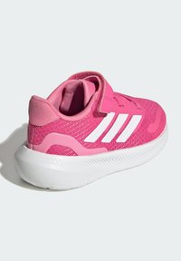 Scarpa atletica rosa con parte superiore in mesh testurizzato, design a tre strisce bianche e colletto imbottito con cinturino a strappo. Suola bianca.