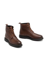 Boots din piele maronie până la gleznă cu șireturi, vârf rotund, guler captusit și finisaj texturat. Dispun de o talpă din cauciuc negru durabilă, cu aderență.
