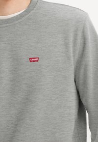 Sudadera gris hecha de una mezcla de algodón, con cuello redondo y un pequeño logo rojo de Levi's bordado en el pecho. Textura suave, ajuste casual.