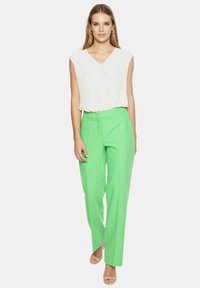 Biała bluzka z dekoltem w serek i krótkim rękawem, zestawiona z jasnooliwkowymi spodniami o wysokim stanie, które mają dopasowany krój i gładką fakturę.