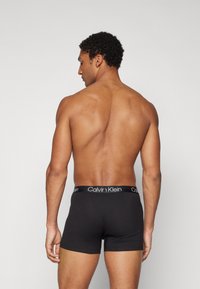 Čierne bavlnené boxerky s kontrastným čierno-bielym pásom Calvin Klein, zobrazené zozadu na modeli.