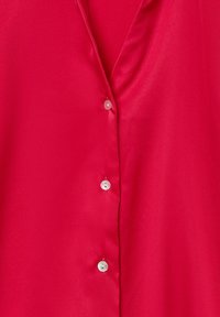 Rote Satinbluse mit tiefem V-Ausschnitt, sechs weißen Knöpfen auf der Vorderseite und glatter Textur. Keine Muster oder zusätzlichen Akzente.