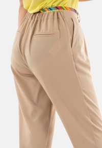 Pantaloni beige a gamba dritta con elastico in vita, caratterizzati da una cintura a righe arcobaleno e due tasche posteriori rifinite in modo pulito.