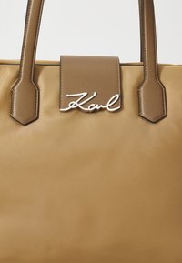 Sac fourre-tout beige en matériau lisse et texturé ; doté d'un rabat amovible avec le logo "Karl" en argent et de poignées structurées.