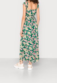 Blommig maxiklänning i grönt med rosa och krämfärgade blommor, med korta ärmar och figursydd midja. Bärs med vita sneakers.