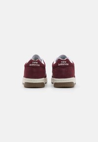 Bordeauxrote Wildleder-Sneaker mit weißen Akzenten und einer beigen Gummisohle. "New Balance"-Logo am Fersenbereich eingestanzt. Niedrig geschnittener Stil.