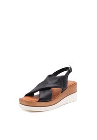 Infradito in pelle nera con cinturini incrociati, soletta color tan e suola in platform bianca. Presenta una cinghia alla caviglia regolabile.
