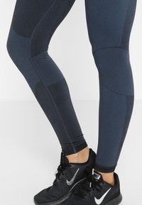 Námořnické sportovní legíny mají různé textury, včetně síťovaných panelů a hladkých částí, s přiléhavým střihem a kontrastními akcenty.