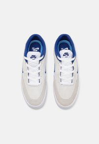 Baltas un gaiši pelēks zamšsneakers ar ziliem akcentiem, aprīkoti ar baltām šņorēm, mīkstinātām apkaklēm un zīmolu uz valkājamo daļu un sāniem.