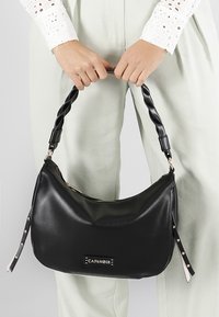 Borsa hobo nera in pelle con manico intrecciato, chiusura con zip e un'etichetta decorativa con logo. Texture liscia con rifiniture lucide.