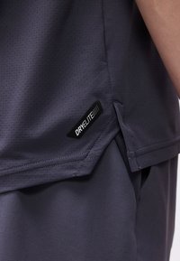 Σκούρο γκρι αθλητικό τοπ από διάτρητο ύφασμα με ετικέτα «DRYELITE» πάνω από λείο σκούρο γκρι παντελόνι ή σορτς.