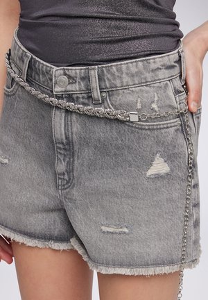 Shorts in denim grigio con orlo sfrangiato, caratterizzati da dettagli rovinosi. Una cintura a catena in argento attaccata aggiunge una texture stratificata e un elemento di design.